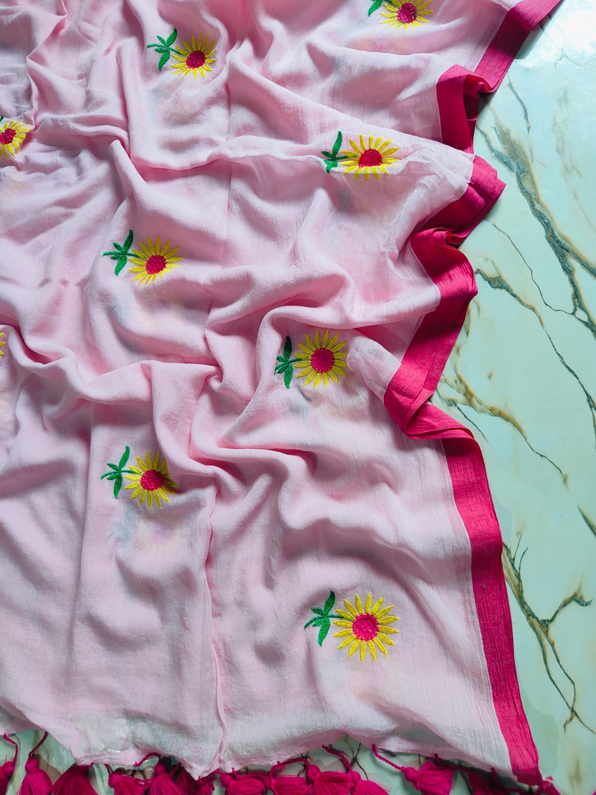Pink fabric with embroidered yellow flowers on a green marble surface